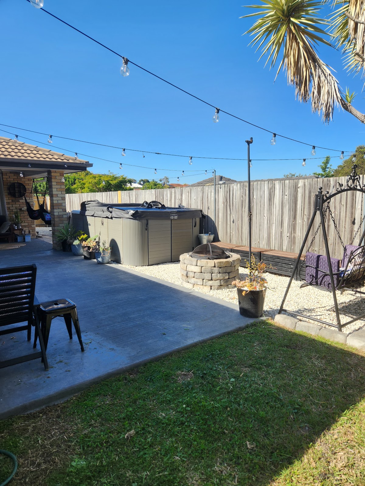 Backyard with festoon lights, spa, fire pit, gravel and lawn