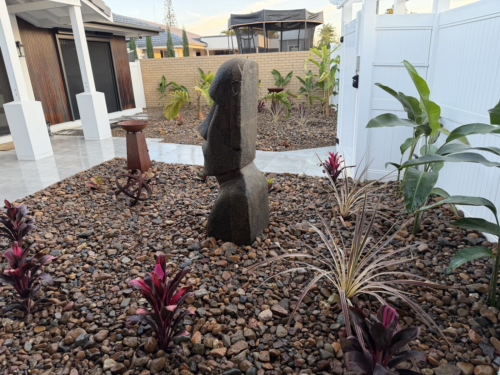 Pebble garden with a stone head statue and red cordylines