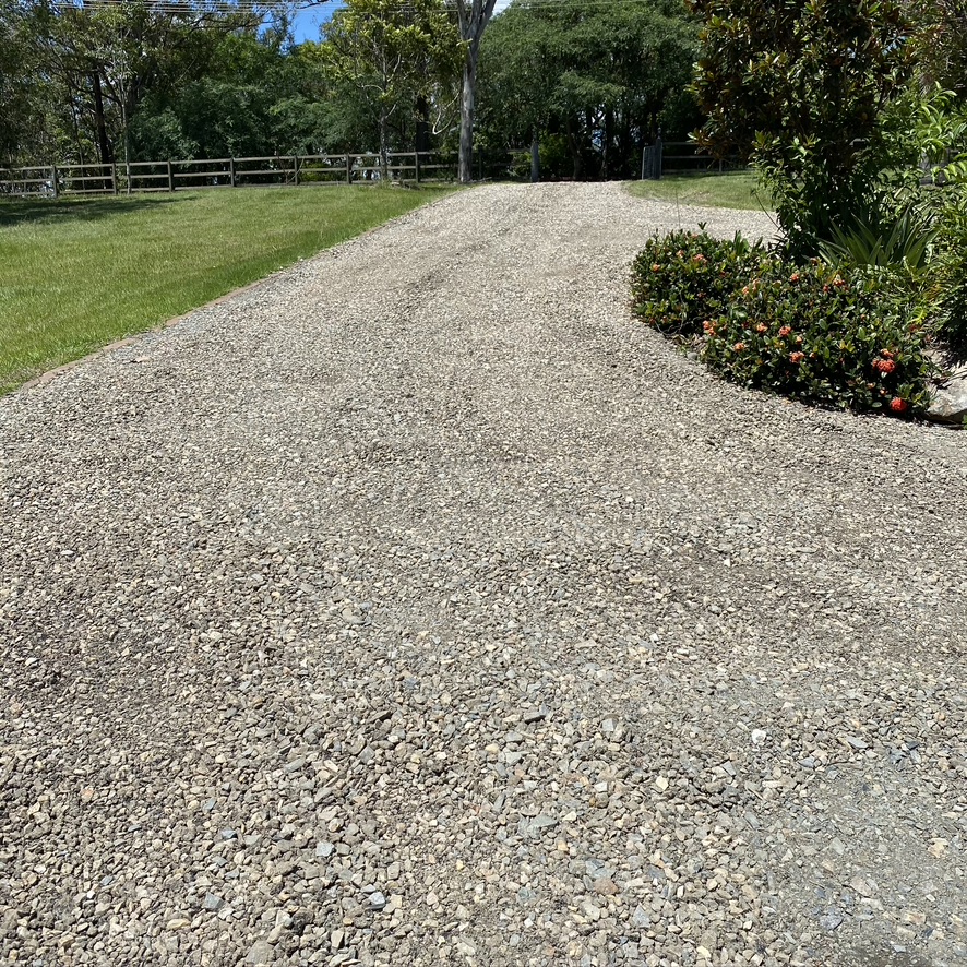 A long gravel driveway sweeping past a flowering garden bed