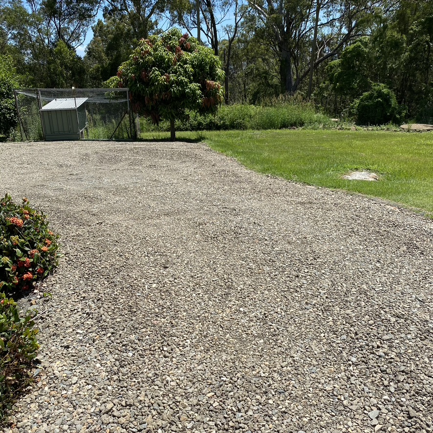A gravelled parking area next to lawn and a flowering hedge